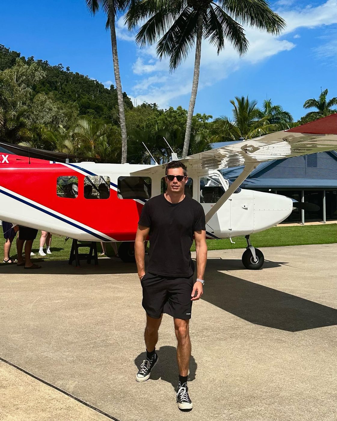 Gio beside a small propeller plane under palm trees